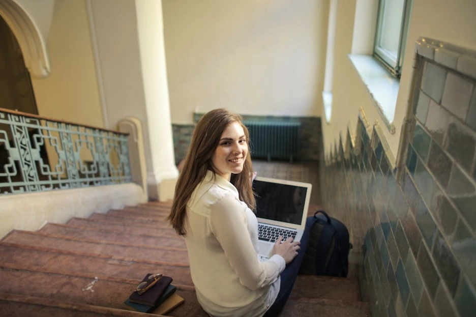 Usměvavá studentka pracující na notebooku v moderní kavárně.